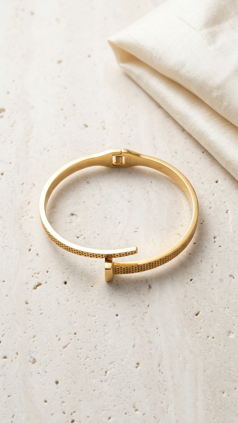 gold-tone nail-shaped wrap bangle with a dotted honeycomb texture, displayed on a soft white silk fabric background