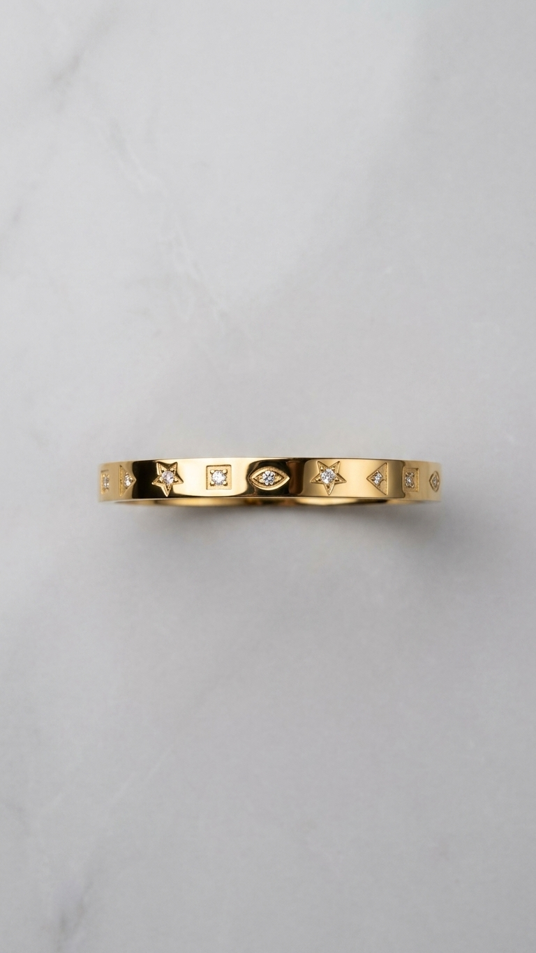 A gold-tone flat bangle featuring star and geometric engravings with small crystals, held against a white fabric background.