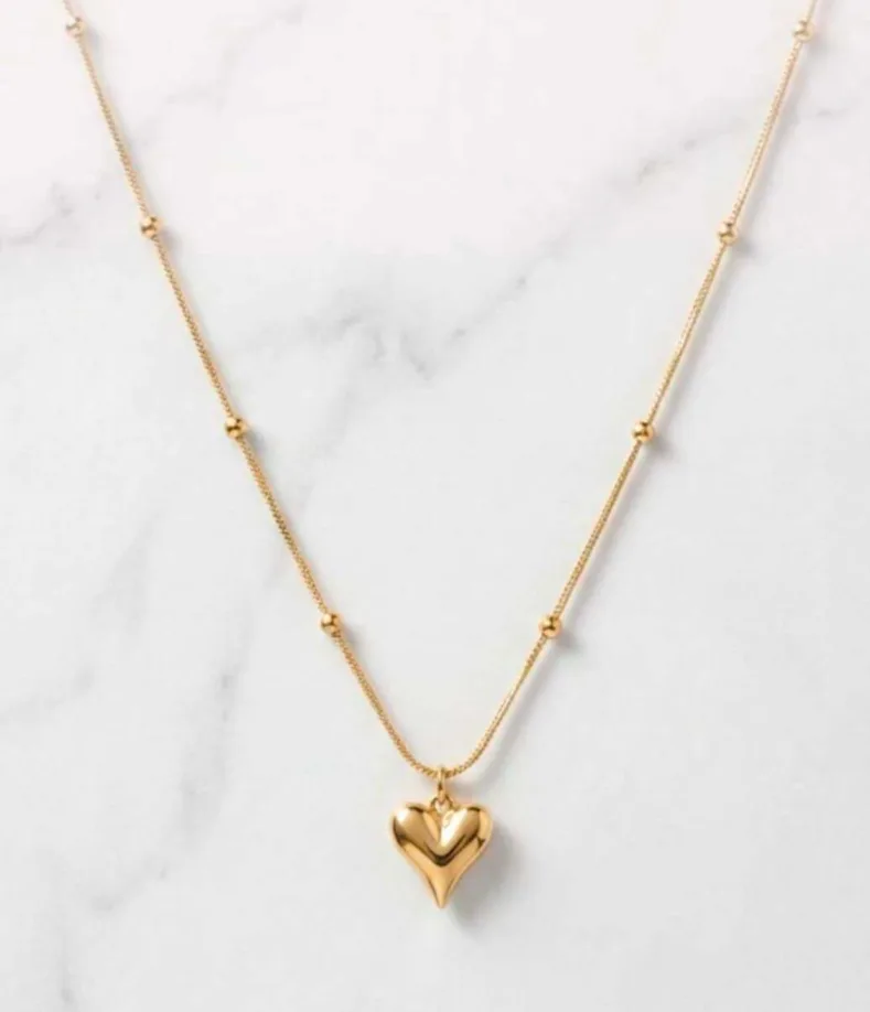 Gold-tone puffed heart pendant on a beaded satellite chain necklace laid on marble