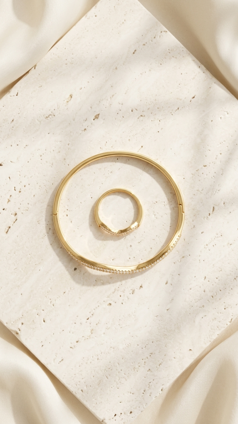gold-tone jewelry set including a wavy bangle and ring, both featuring two rows of densely set white crystals, photographed on a shimmering grey fabric.