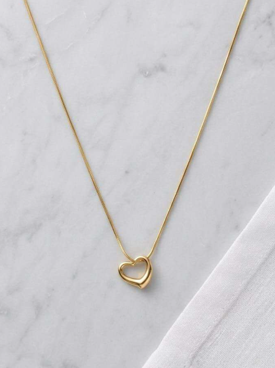Gold-tone open heart pendant necklace on a fine snake chain laid on marble