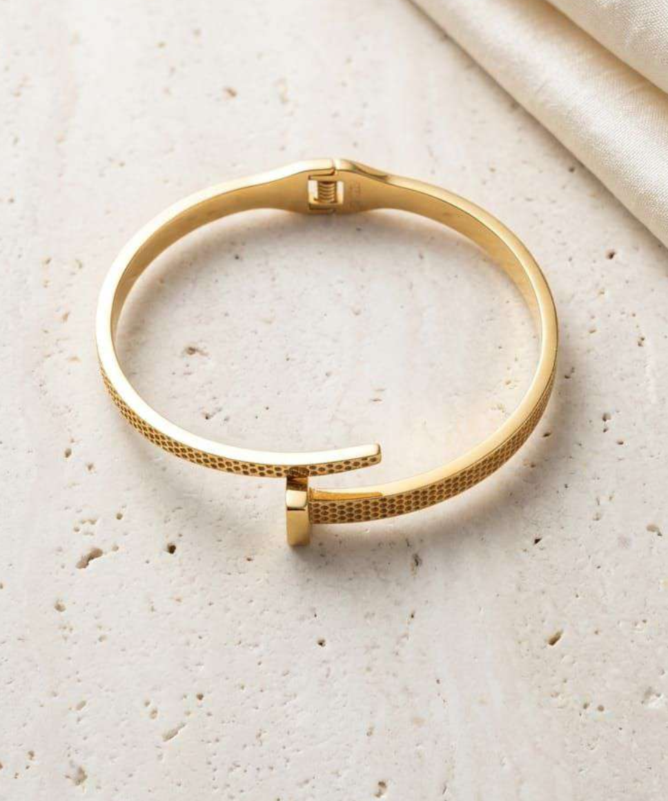Gold-tone textured nail-shaped cuff bracelet shown flat on marble surface