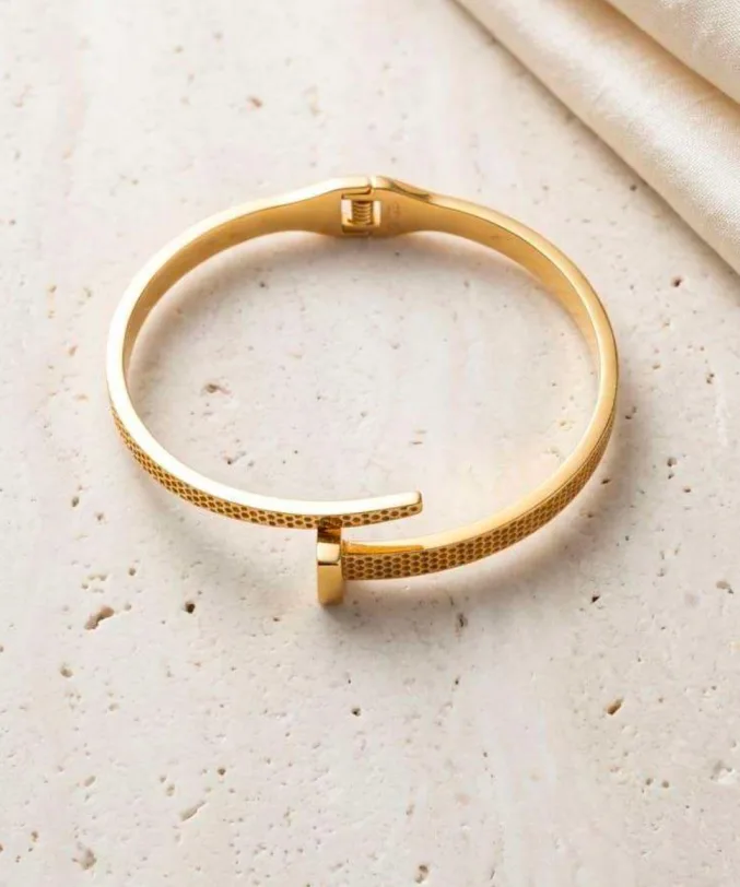 Gold-tone textured nail-shaped cuff bracelet shown flat on marble surface
