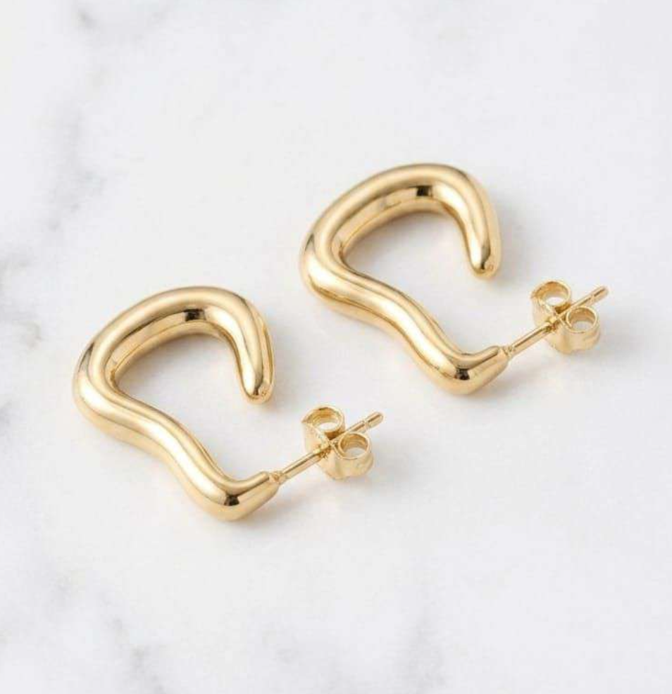 Gold-tone sculptural wave mini hoop earrings on marble background