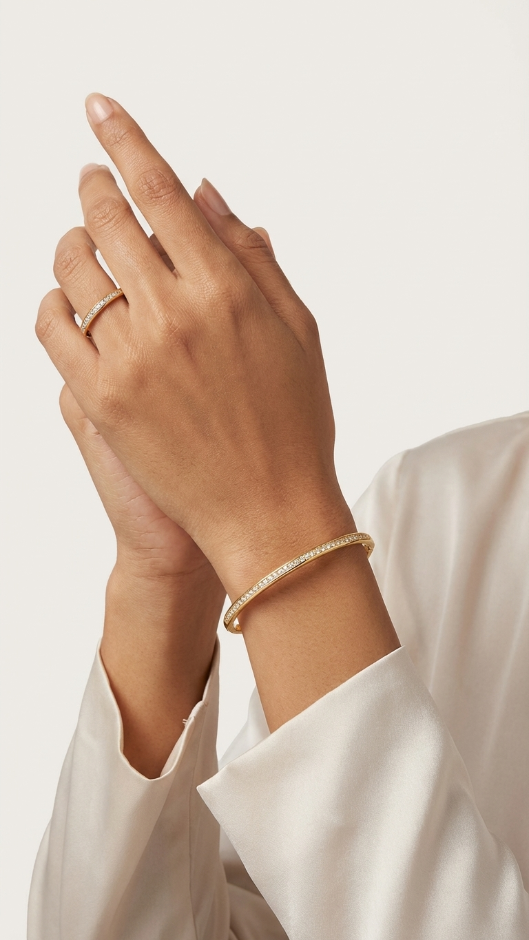 A minimalist gold-tone jewelry set featuring a thin circular bangle and a matching ring, both with a single row of small white crystals, placed on a silver-grey fabric.