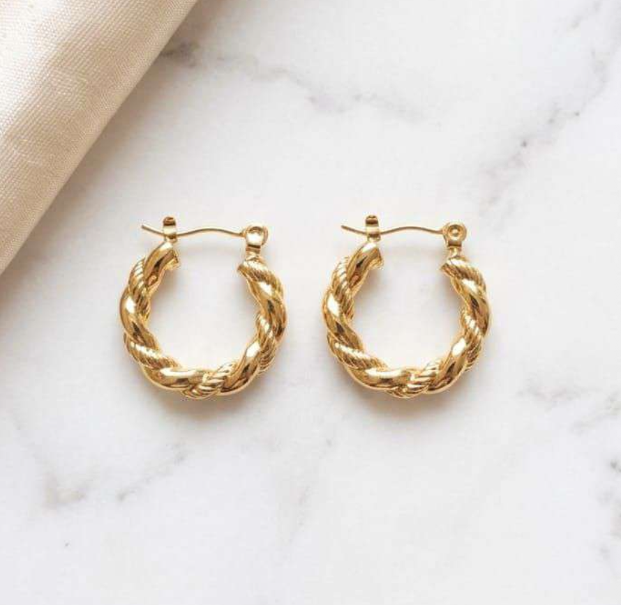 Gold-tone twisted rope texture hoop earrings on marble surface