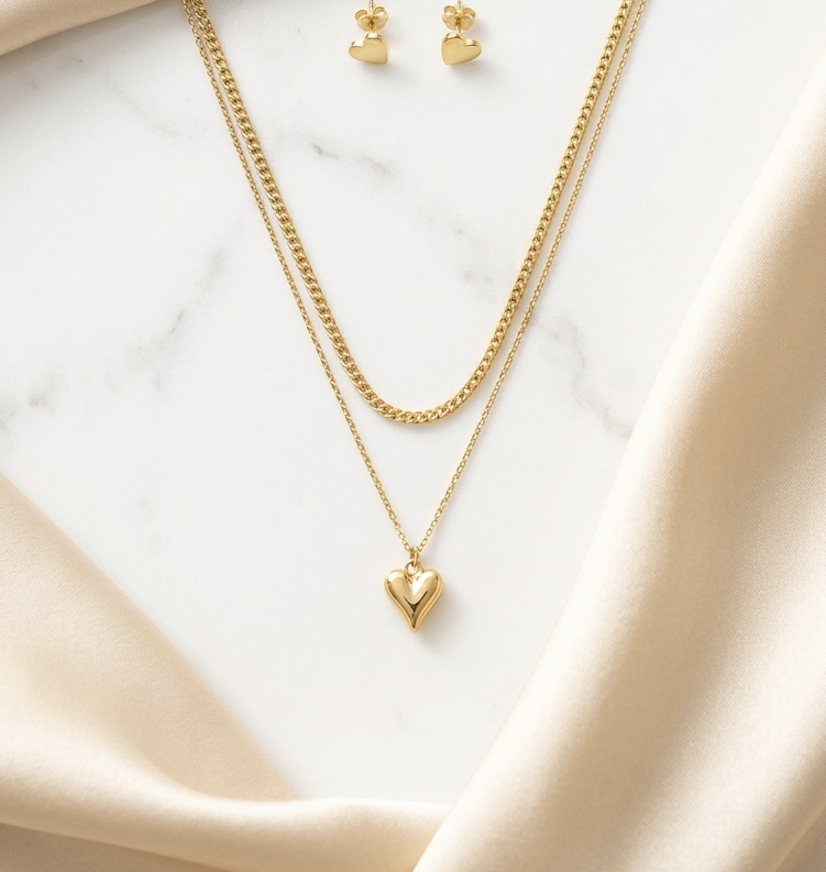 Elegant double layer gold heart pendant necklace with matching heart stud earrings on satin background