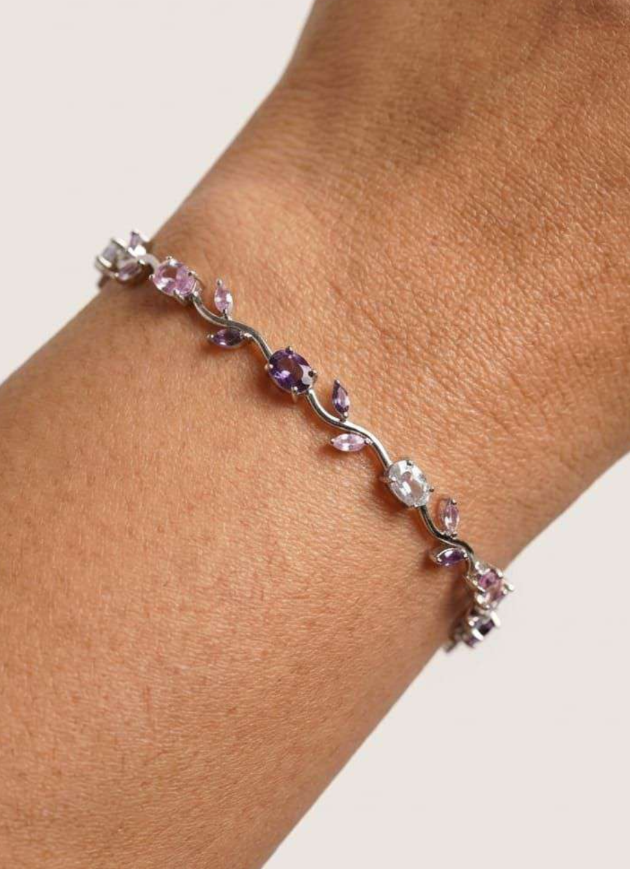Silver-tone tennis bracelet with pink and purple gemstones in a vine design, worn on wrist