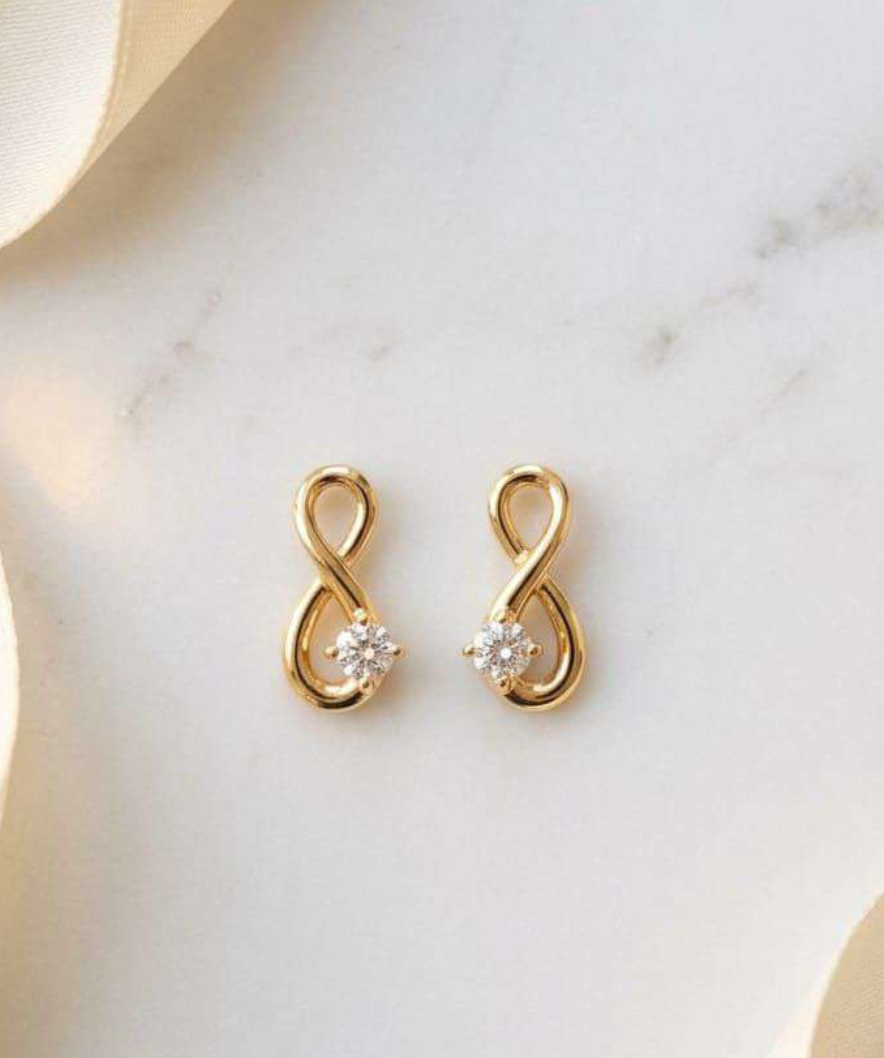 Gold-tone infinity symbol stud earrings with cubic zirconia accent on marble background
