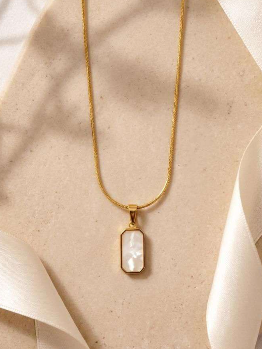 Gold-tone rectangular mother-of-pearl pendant necklace on snake chain, hung against fabric