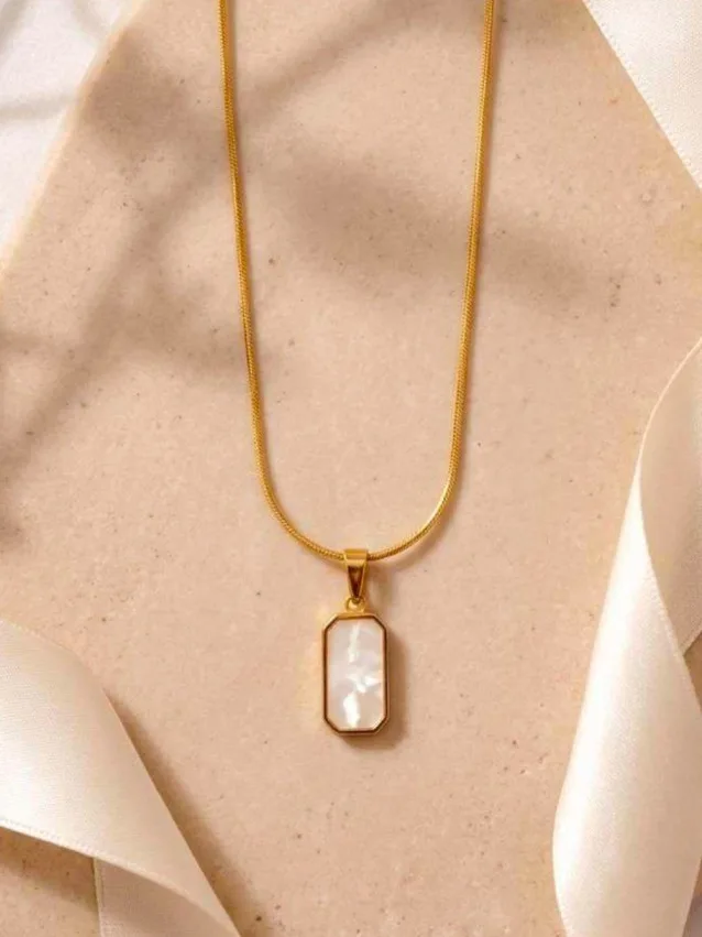 Gold-tone rectangular mother-of-pearl pendant necklace on snake chain, hung against fabric