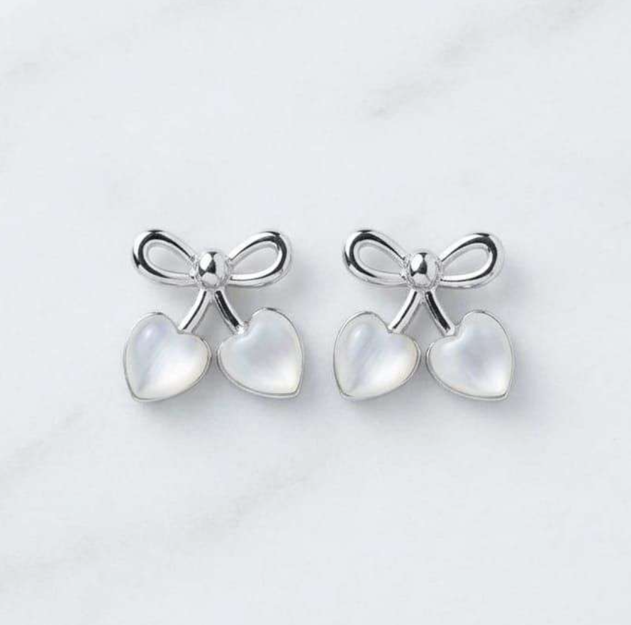 Silver-tone bow stud earrings with two mother-of-pearl heart charms on marble background