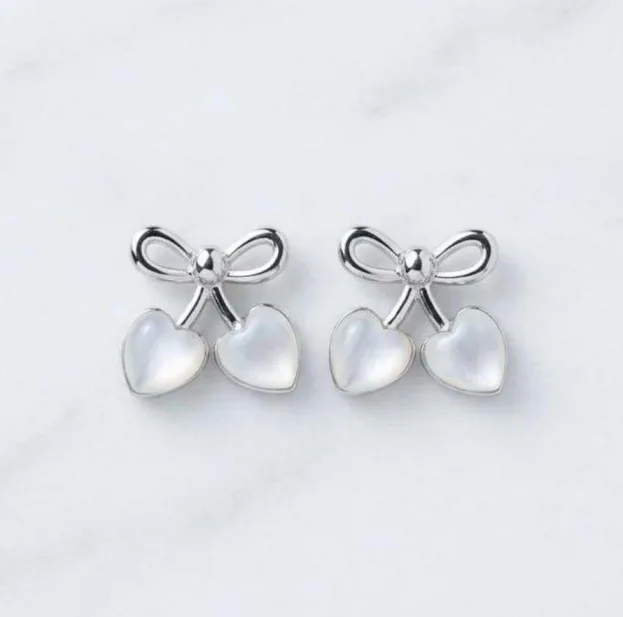 Silver-tone bow stud earrings with two mother-of-pearl heart charms on marble background