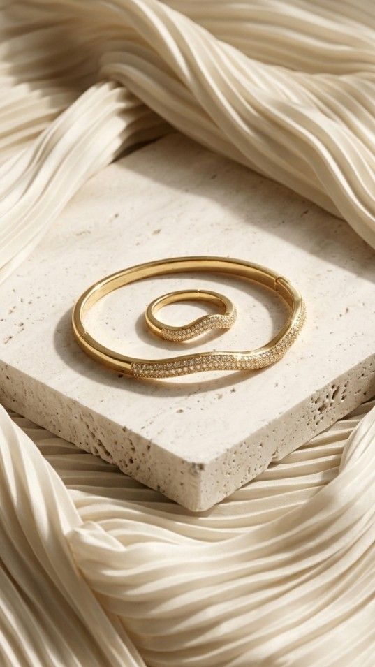 gold-tone jewelry set including a wavy bangle and ring, both featuring two rows of densely set white crystals, photographed on a shimmering grey fabric.