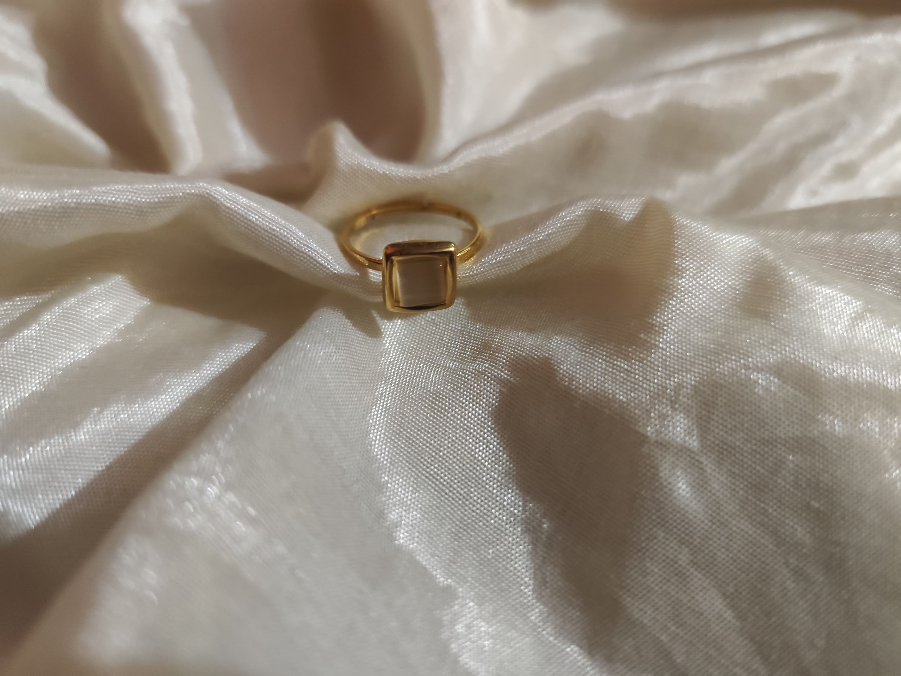 Minimal gold ring with square stone set on satin fabric, elegant and modern jewelry for women