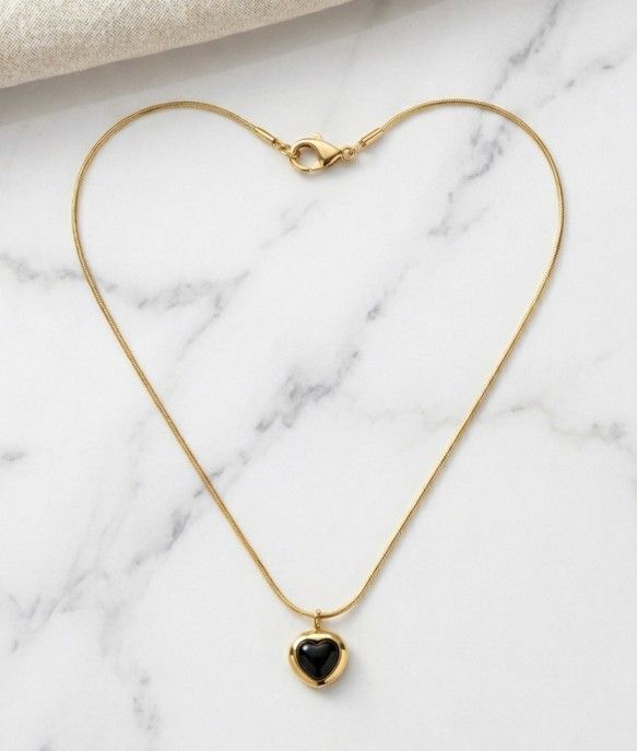 Gold chain necklace with black heart-shaped pendant on satin fabric, elegant and stylish jewelry for women