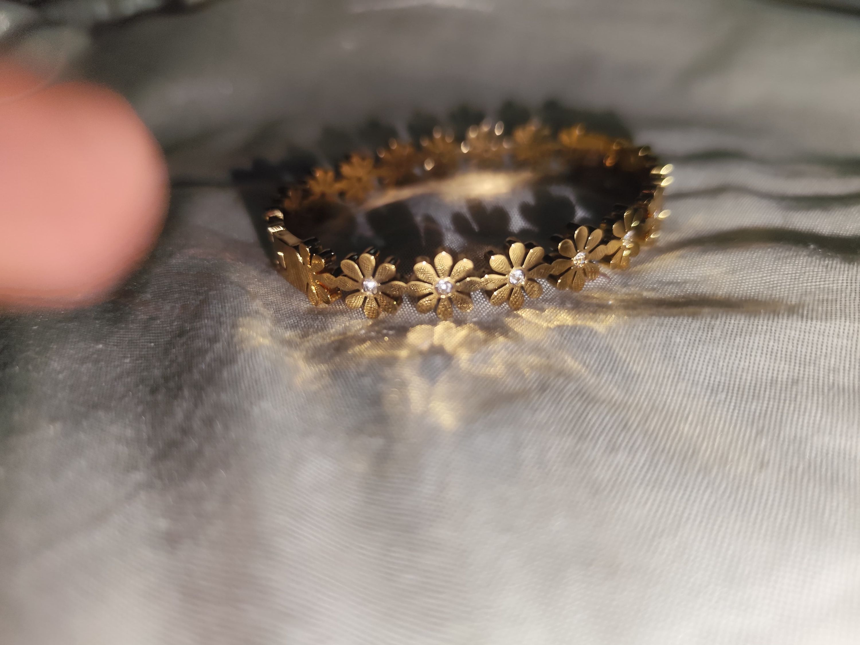 Close-up shot of a gold daisy-shaped bracelet with small crystals in the center of each flower, resting on a shimmering fabric background.