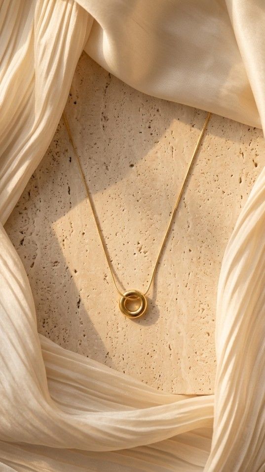 Minimalist gold necklace with small circular ring pendant on satin background
